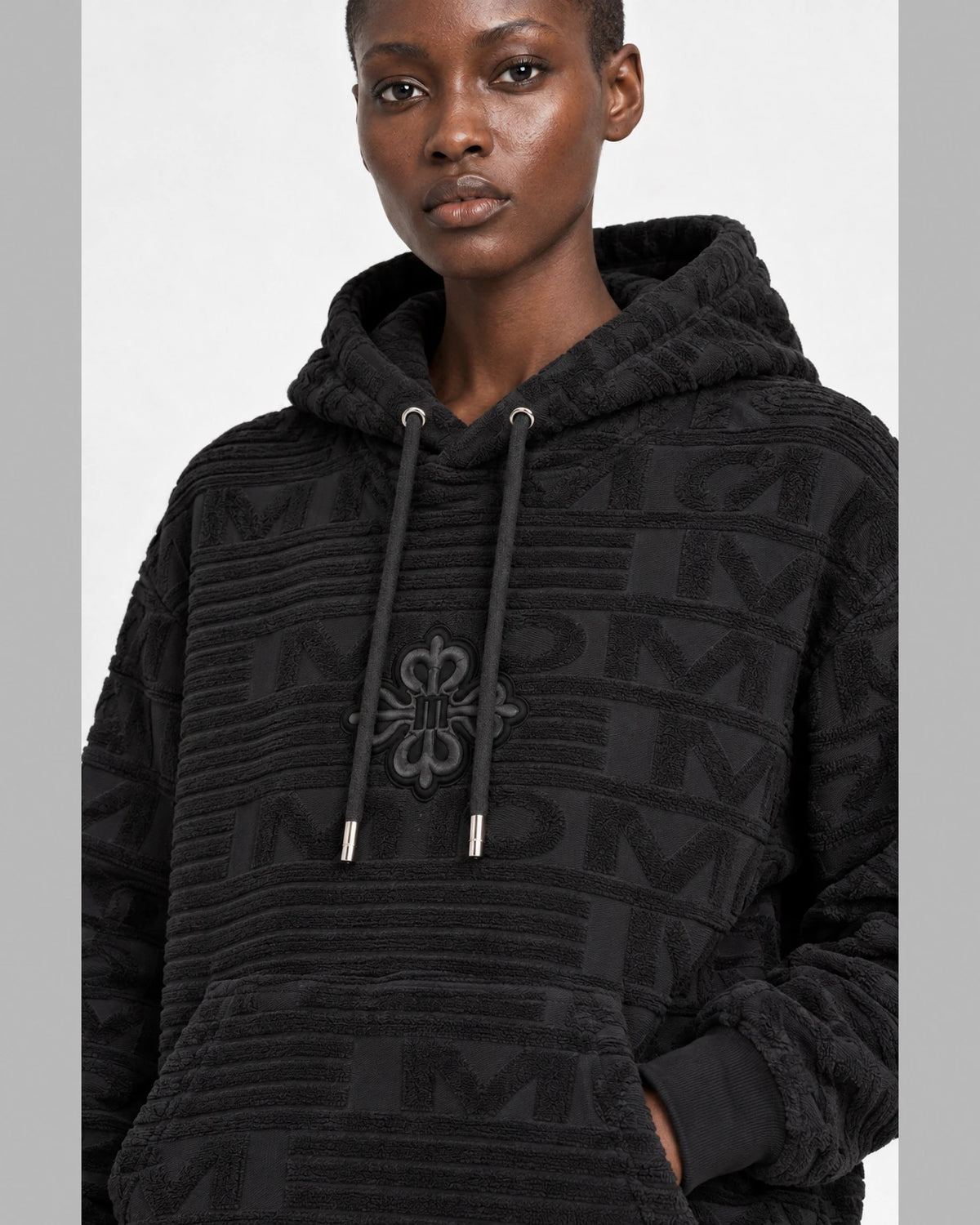 MOMANI Emblem Terry Hoodie in Black, worn by a model, close detail